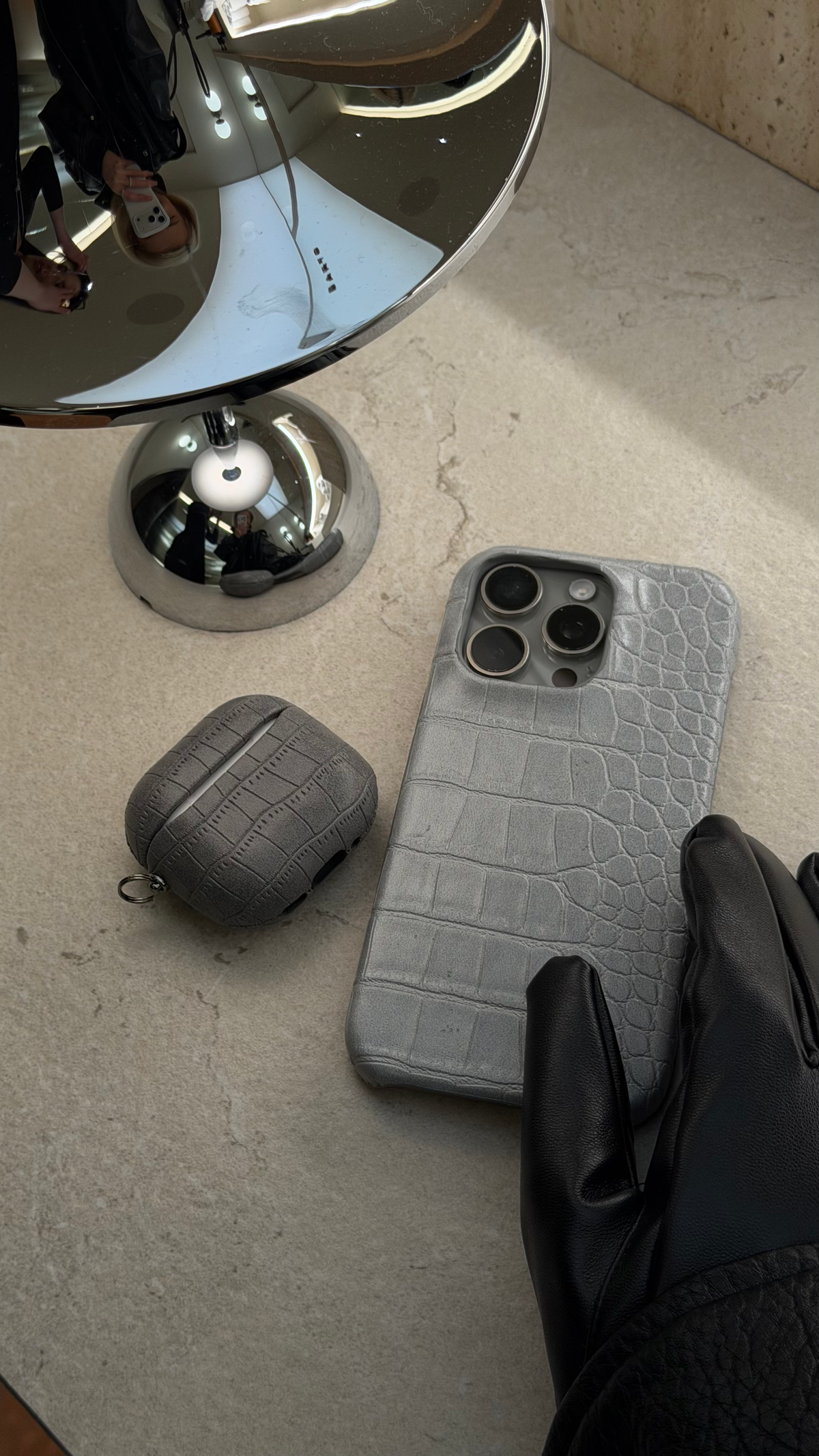 iPhone і AirPods у сірих чохлах із фактурою під шкіру крокодила біля настільного дзеркала