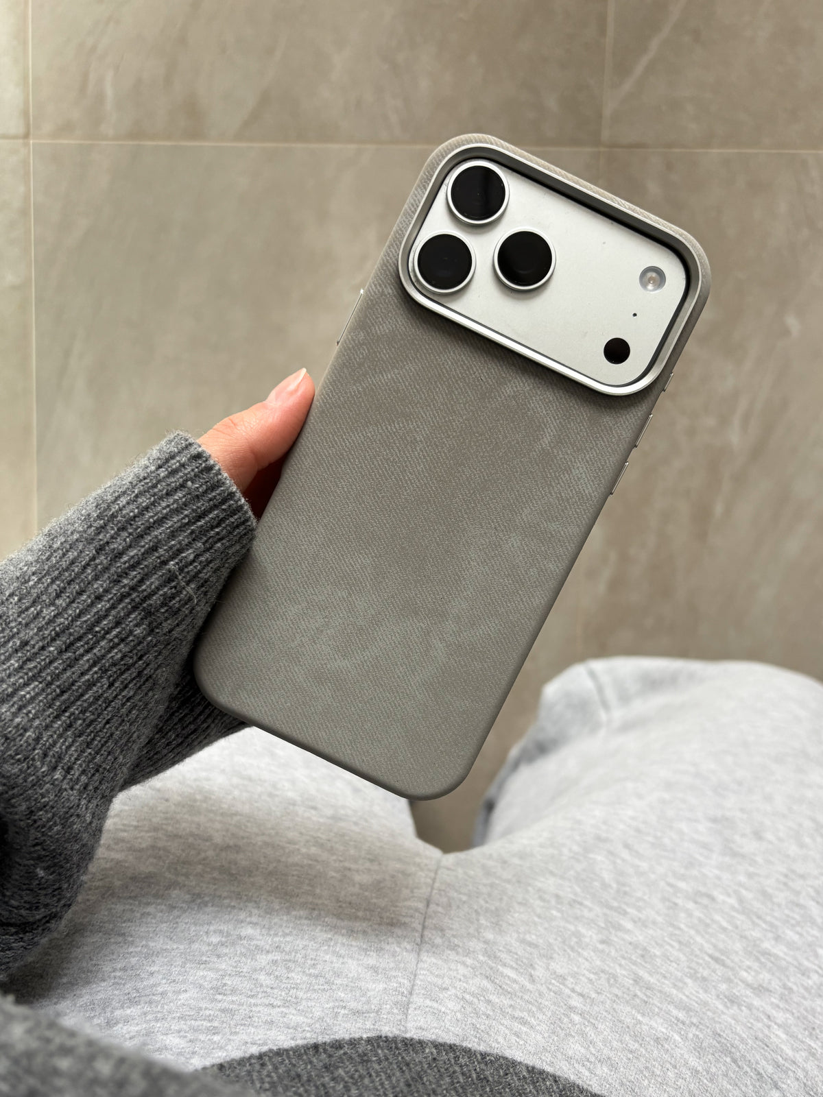 Сірий чохол на iPhone у руці на тлі плитки й сірого трикотажу