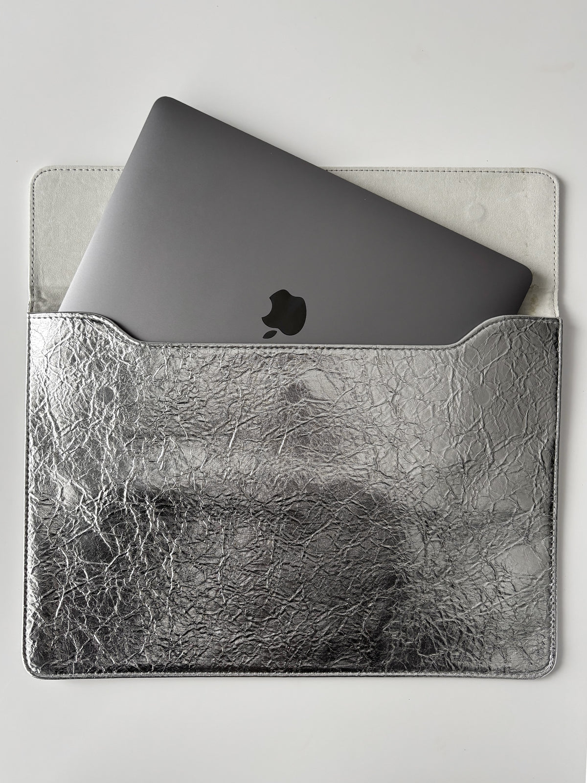 Сріблястий конверт «Текстурне сяйво» з наполовину вставленим MacBook