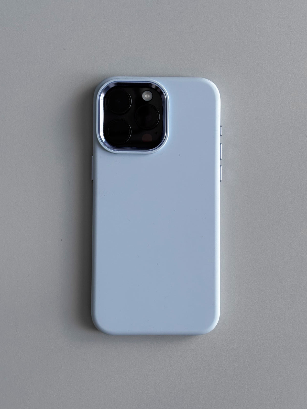 Світло-блакитний чохол на iPhone з квадратним вирізом під камеру — вигляд ззаду на сірому тлі
