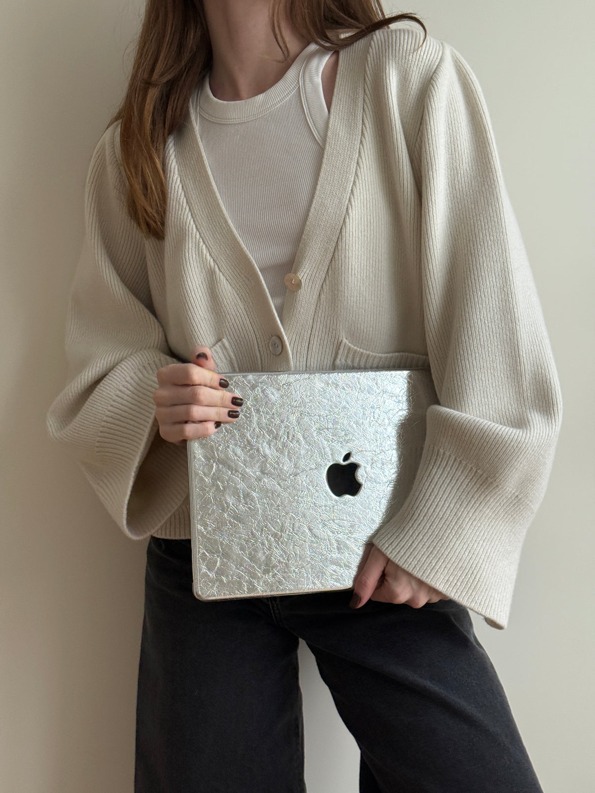 Жінка в кремовому кардигані тримає MacBook у сріблястому чохлі «Текстурне сяйво»