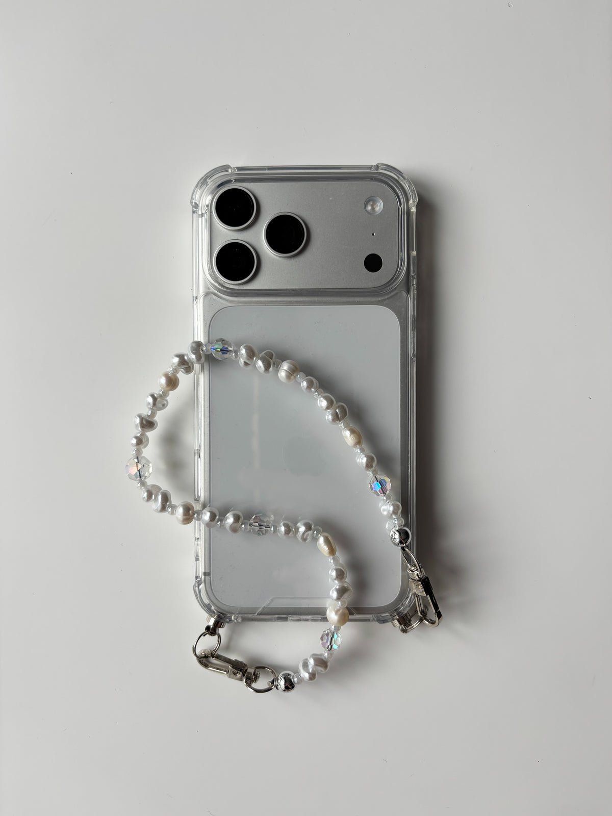 Короткий ланцюжок Crystal Pearl, покладений петлею на телефон у прозорому чохлі