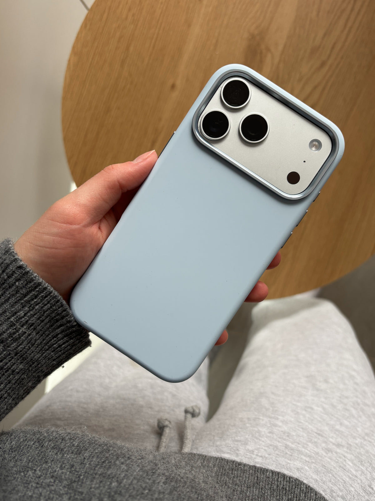 Світло-блакитний чохол на iPhone у руці на тлі дерев’яного столу