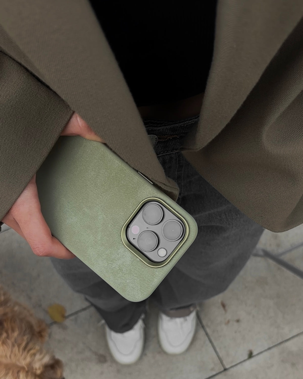 Оливковий чохол «Замшева м’якість» на iPhone у руці на тлі коричневого жакета й джинсів