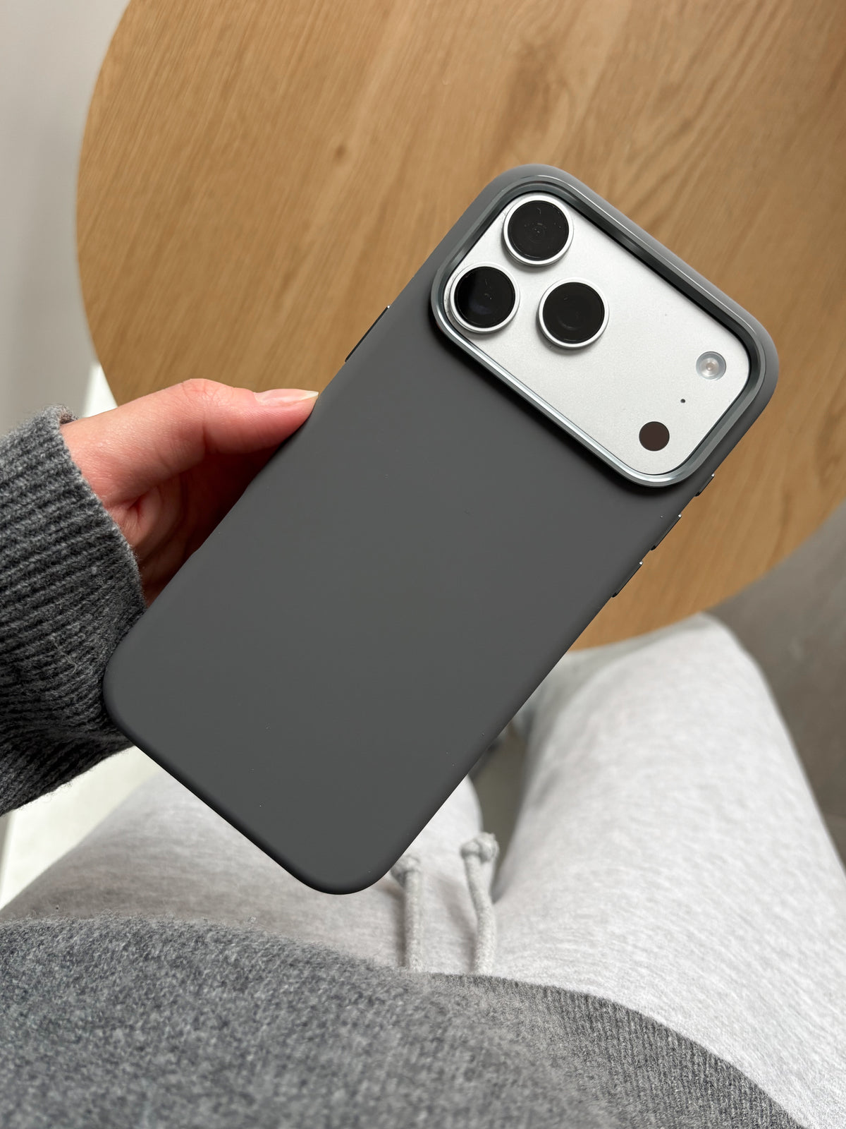 Графітовий чохол «Металеві деталі» на iPhone у руці на тлі дерев’яного столу