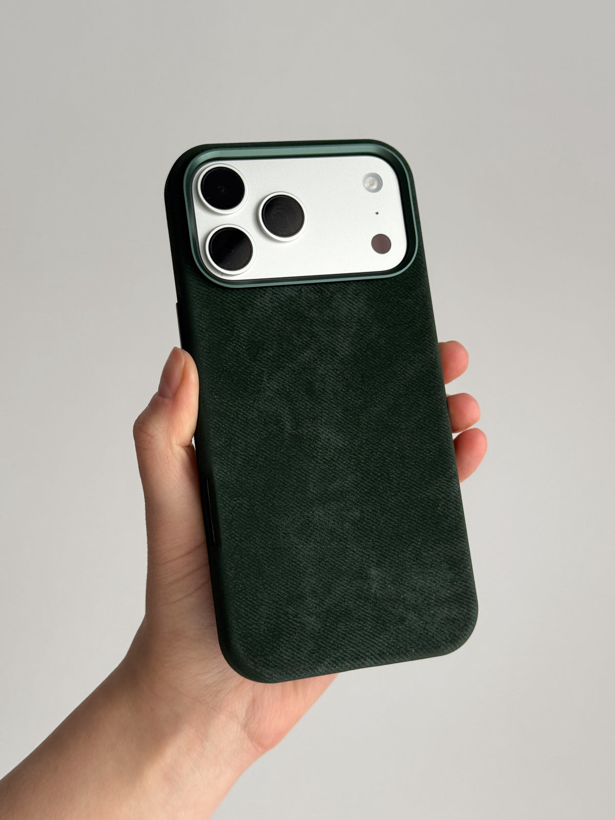 Темно-зелений чохол на iPhone зі світлим блоком камер у руці