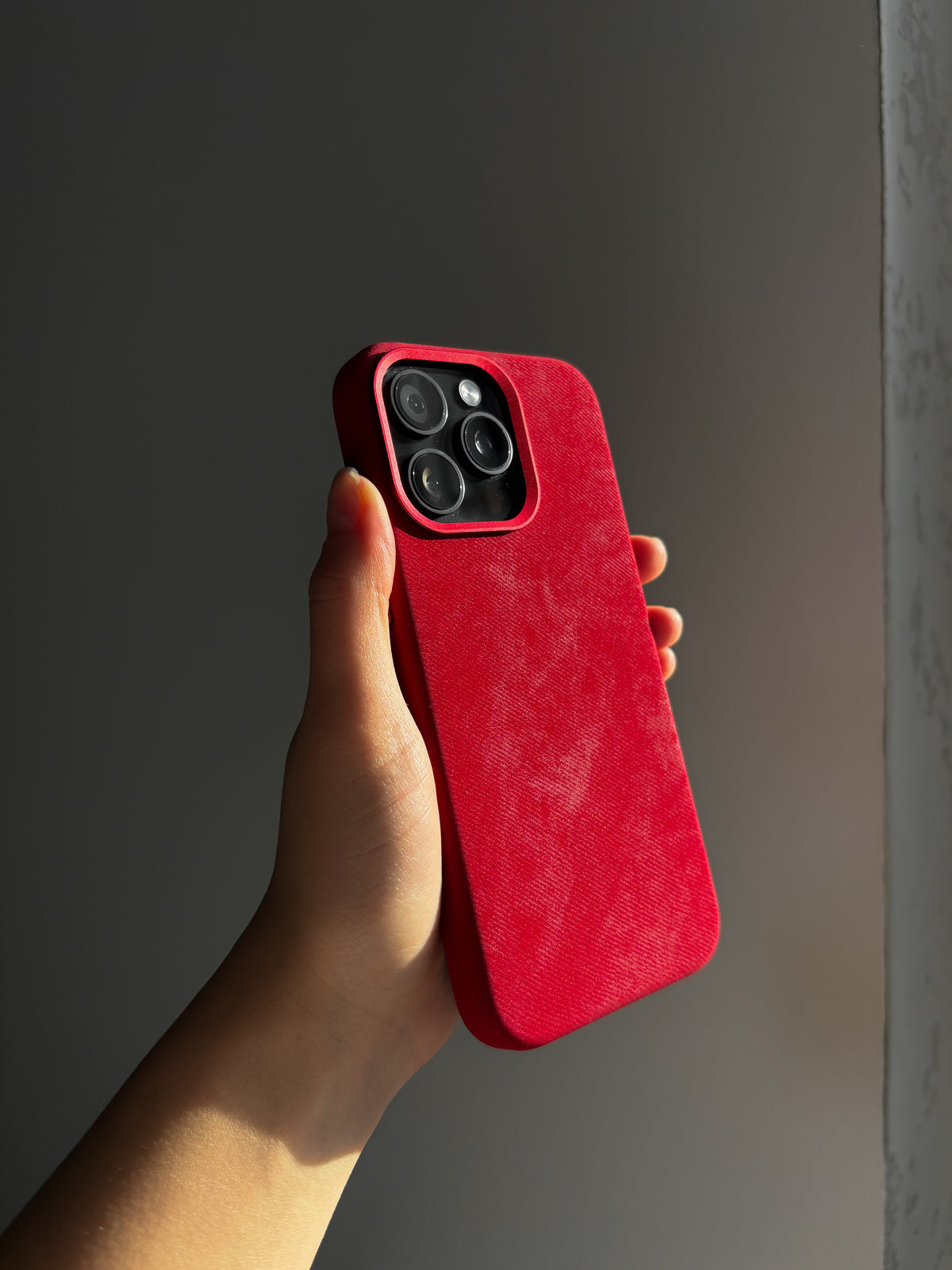 Червоний чохол на iPhone у руці вертикально на темному тлі