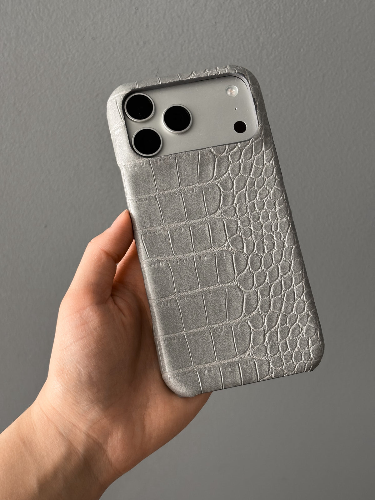 Сірий чохол Gator Skin на iPhone у руці на сірому тлі