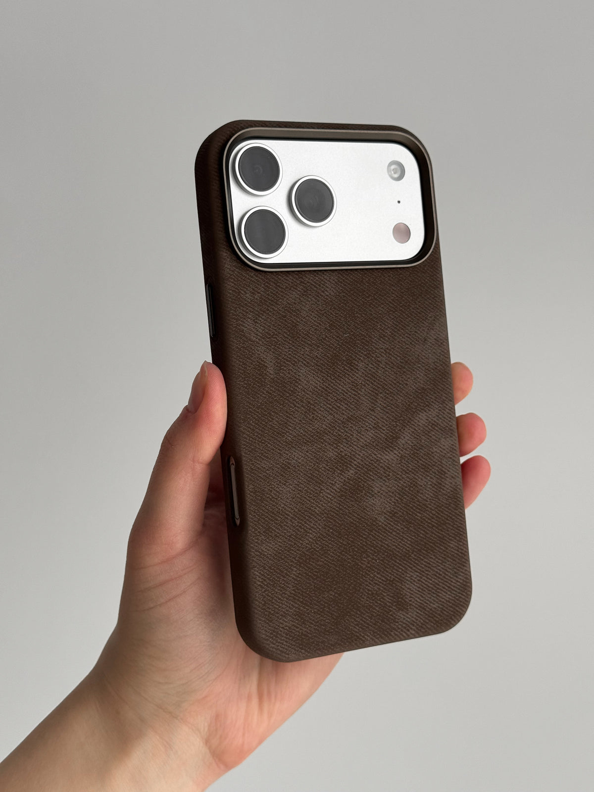Коричневий чохол на iPhone зі світлим блоком камер у руці