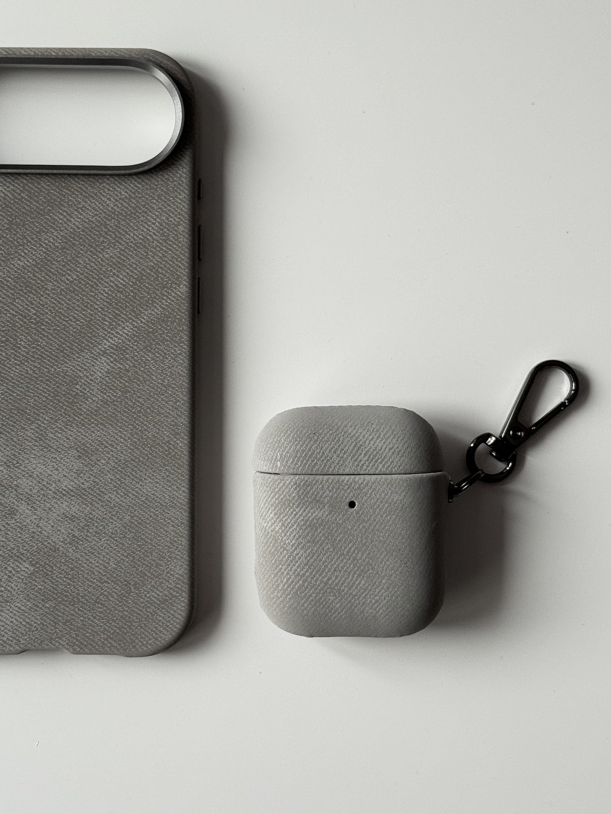 Сірий чохол «Замшева м’якість» на вужчому кейсі AirPods поруч із чохлом для iPhone