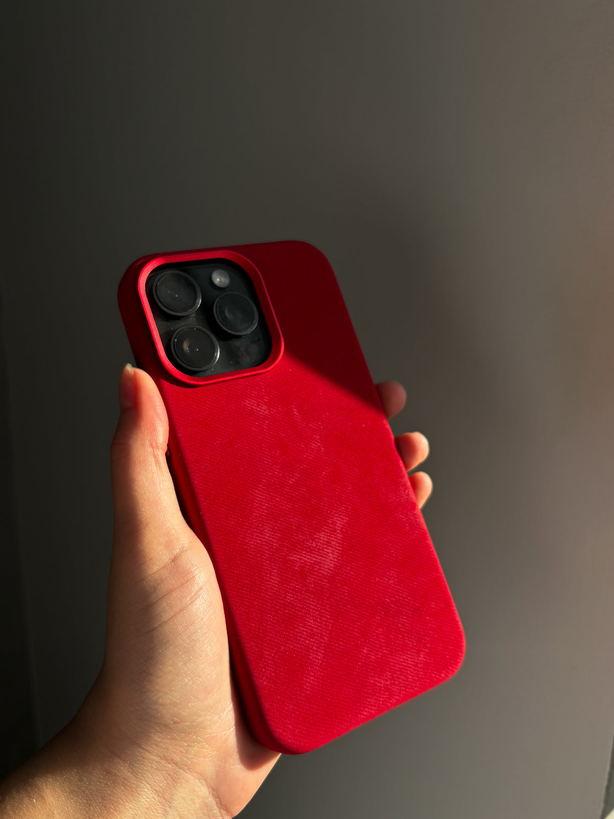 Червоний чохол на iPhone у руці крупним планом на темно-сірому тлі