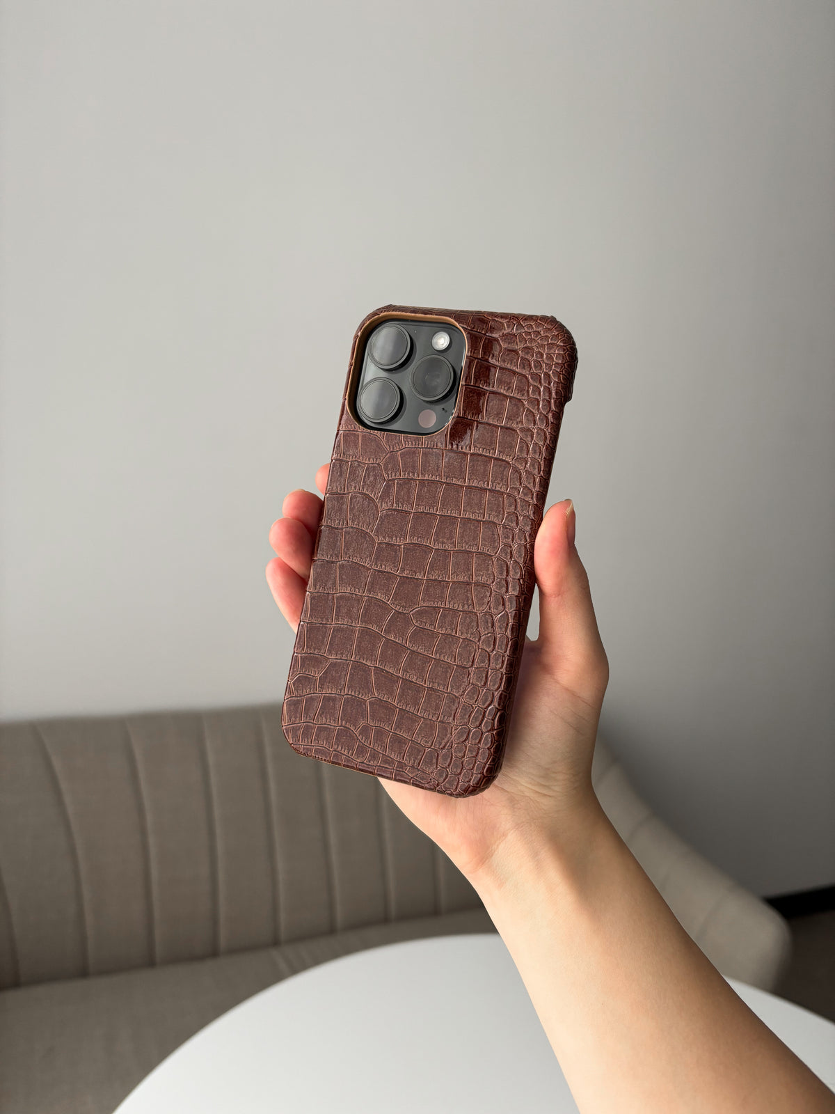 Коньячно-коричневий чохол Gator Skin на iPhone у витягнутій руці на тлі крісла