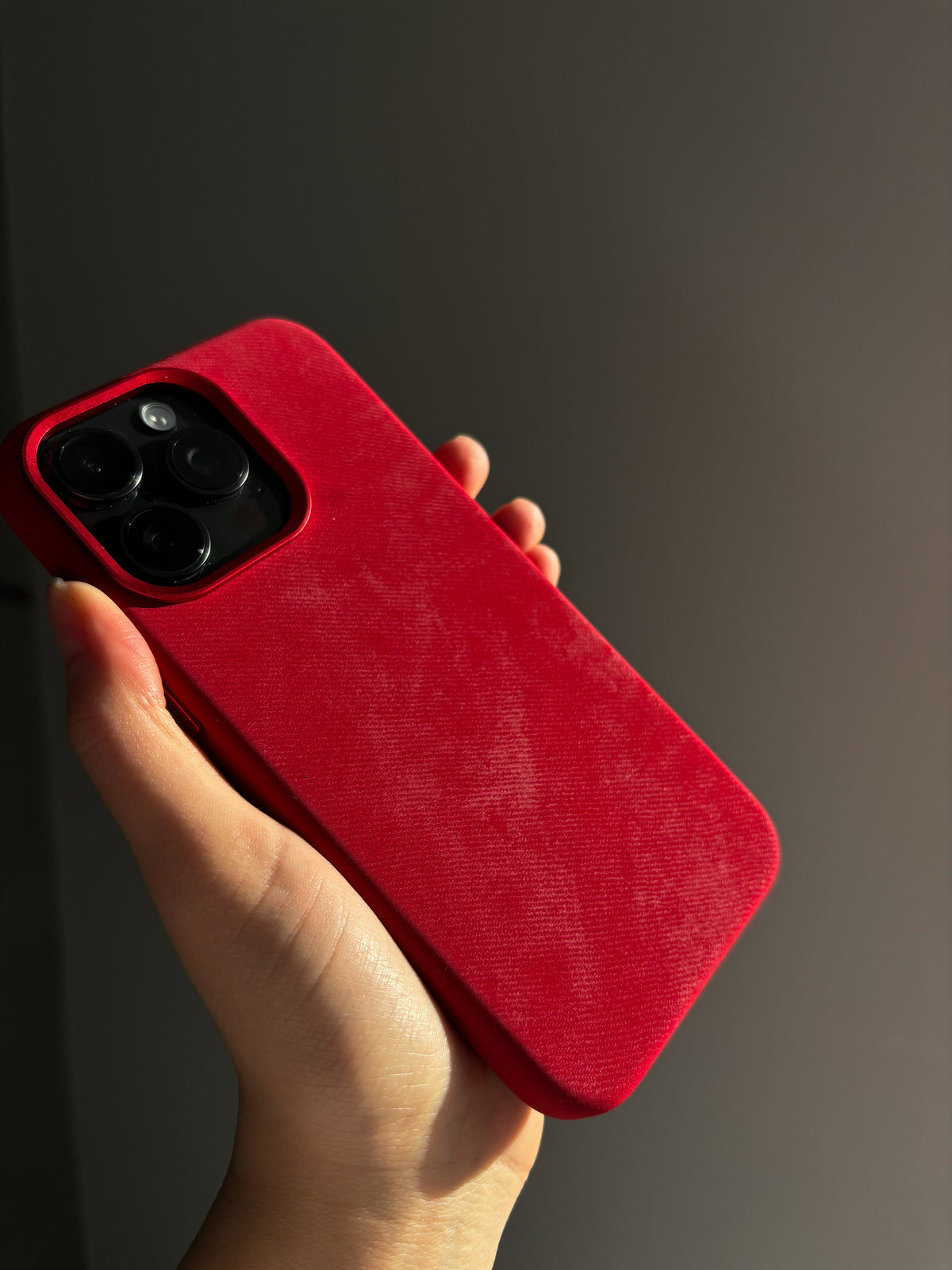 Червоний чохол на iPhone у руці під нахилом на темному тлі