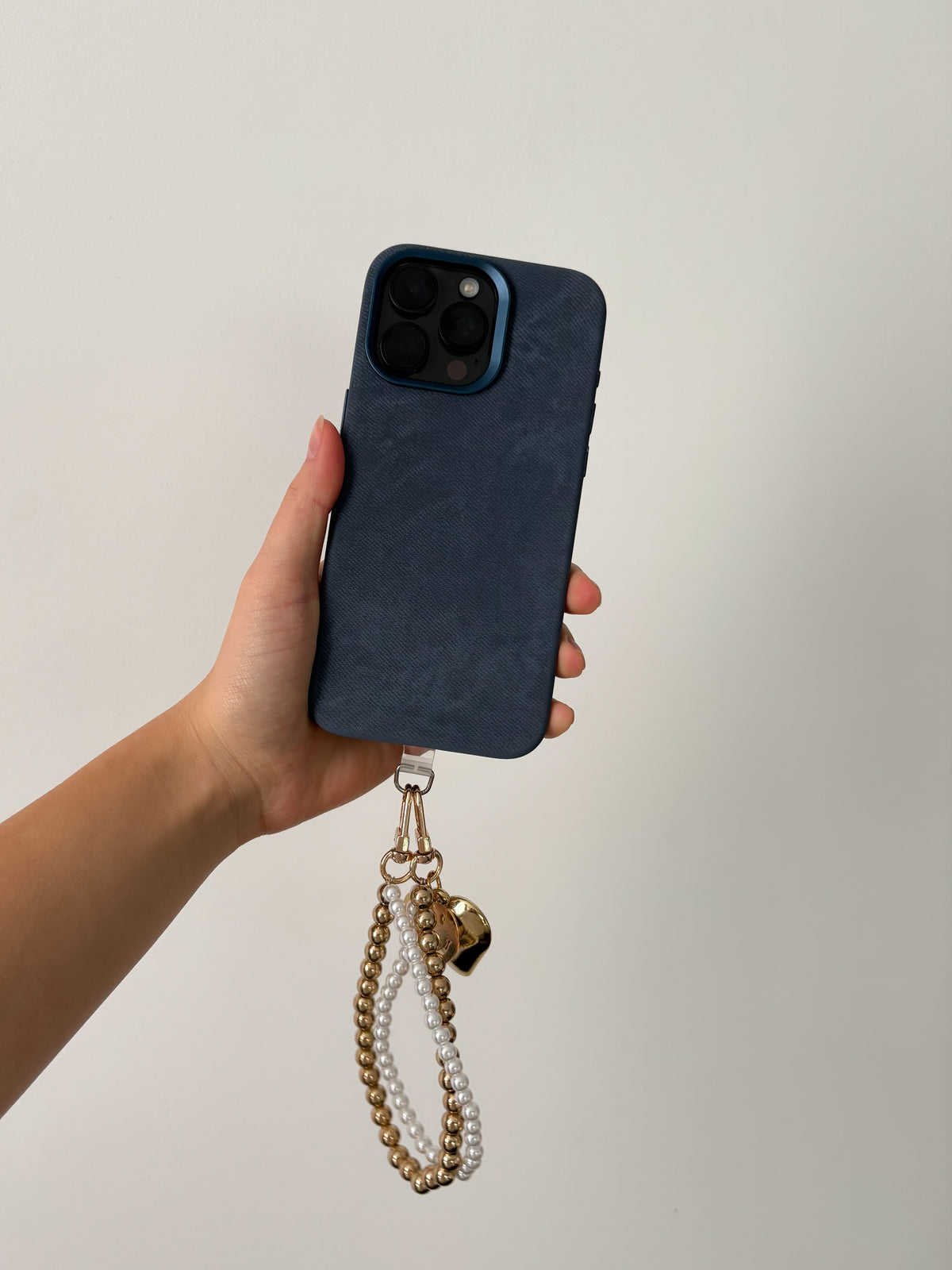 Синій чохол на iPhone у руці з перлинно-золотистим ремінцем-підвіскою