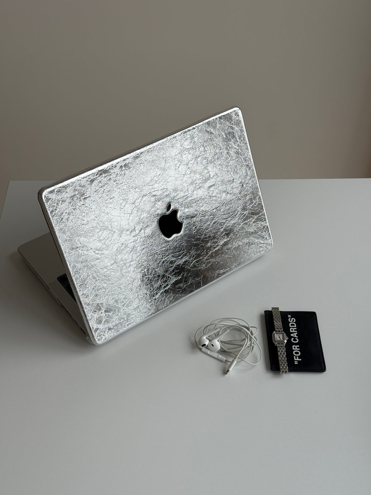 Сріблястий чохол-накладка «Текстурне сяйво» для MacBook зі зім’ятою фактурою поруч із навушниками й годинником