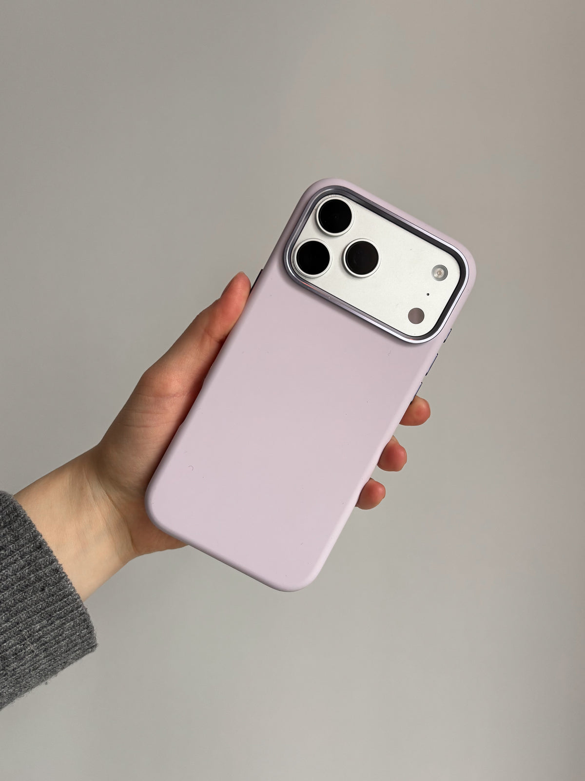 Лавандово-рожевий чохол на iPhone у руці в сірому рукаві