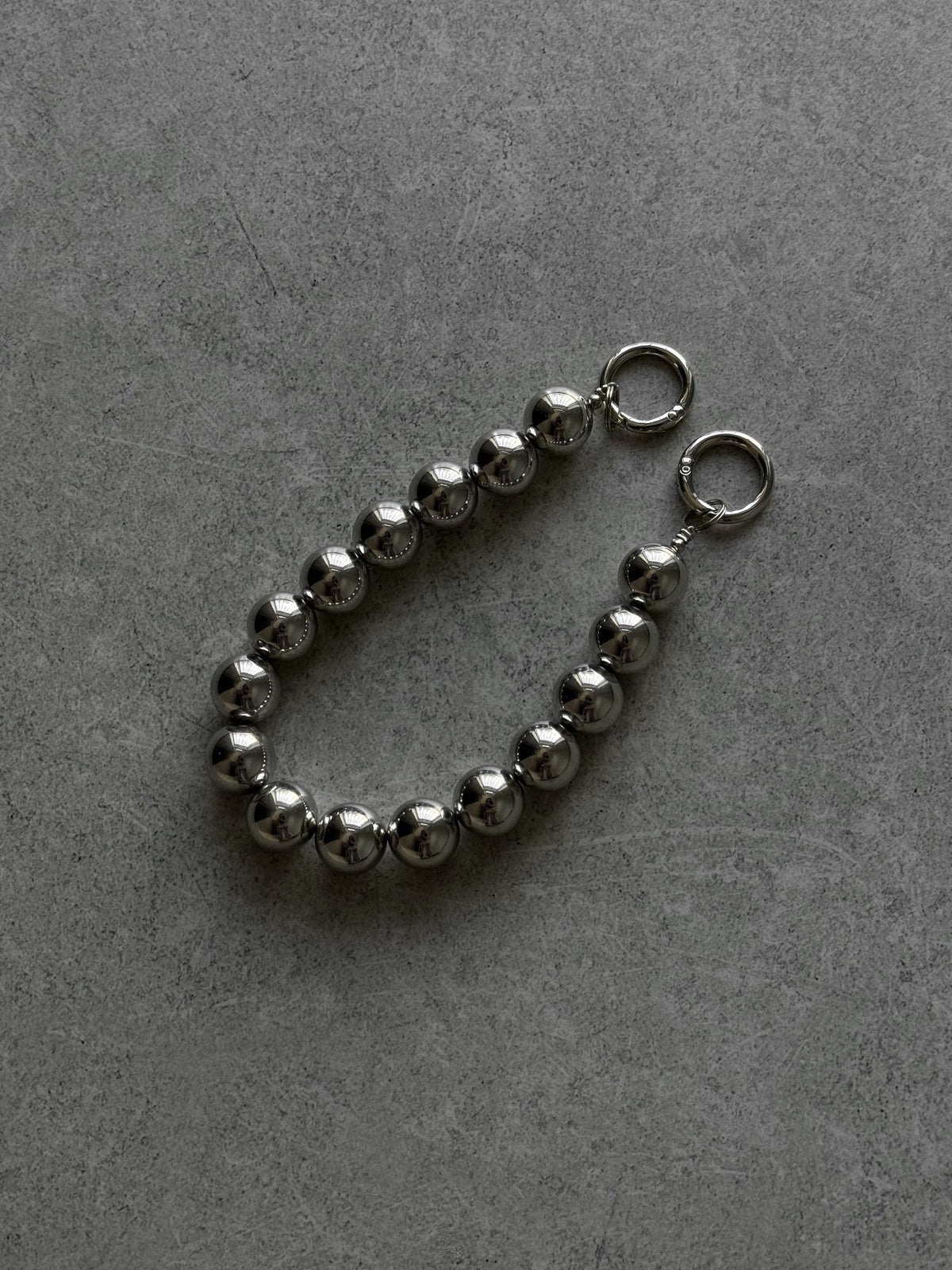Короткий ланцюжок Mirror Beads із великих дзеркальних сріблястих кульок із кільцями-застібками на сірому бетоні