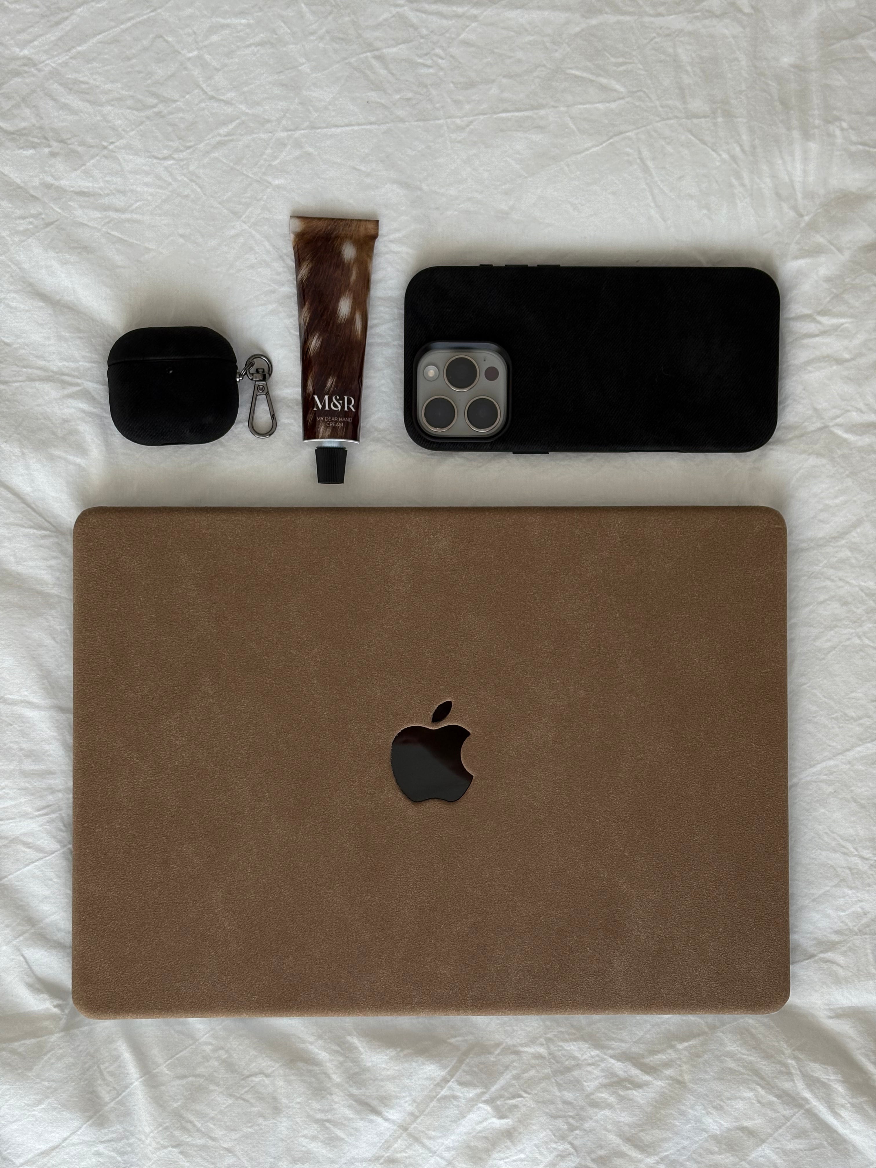 Коричневий чохол «Замшева м’якість» для MacBook на білій тканині поруч з iPhone і навушниками в чорних чохлах