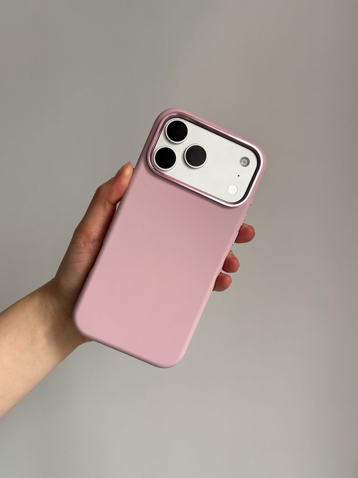 Рожевий чохол «Металеві деталі» на iPhone у руці на сірому тлі