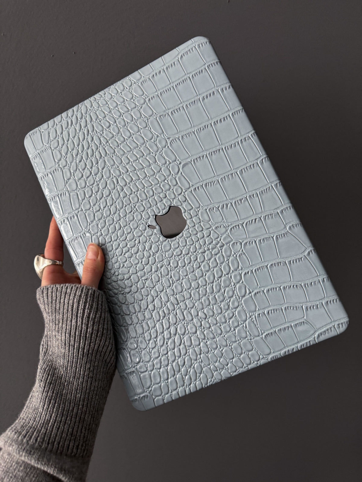 Блакитний чохол Gator Skin на MacBook у руці на темному тлі