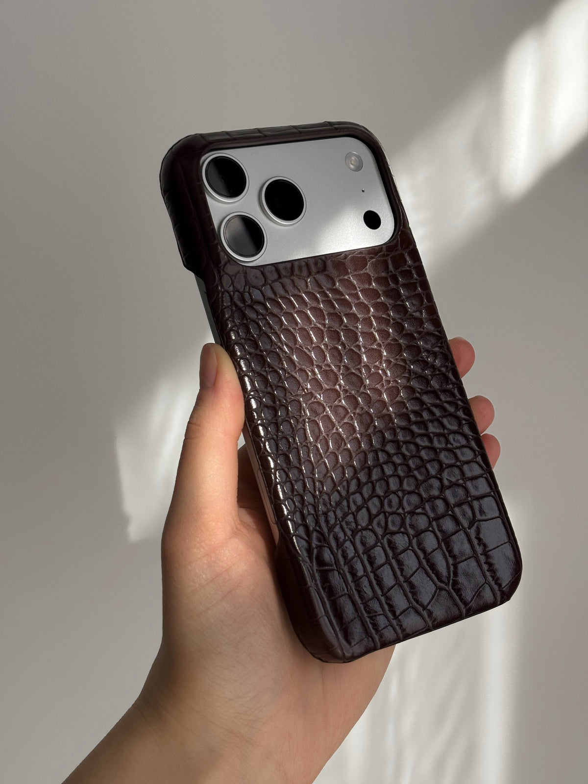 Шоколадний чохол Gator Skin на iPhone у руці в сонячному світлі
