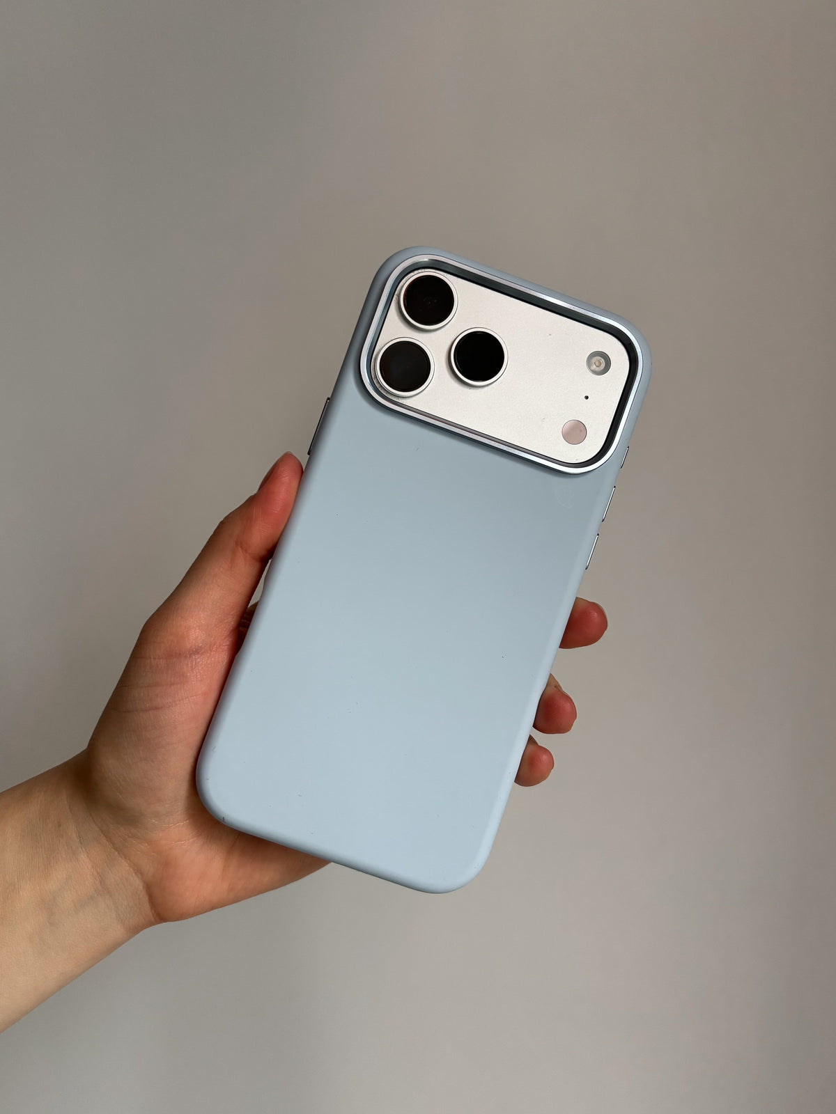 Світло-блакитний чохол на iPhone у руці, вертикально на світлому тлі