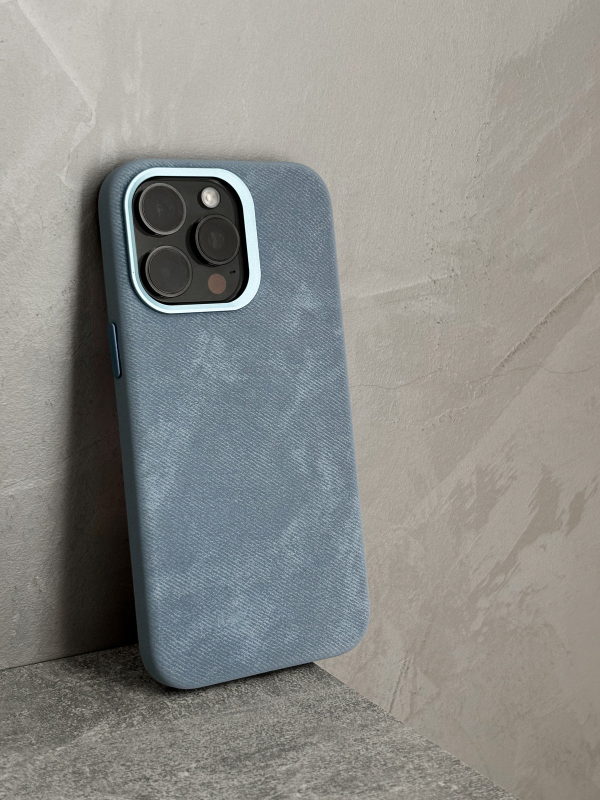 Блакитний чохол «Замшева м’якість» на iPhone стоїть біля бетонної стіни