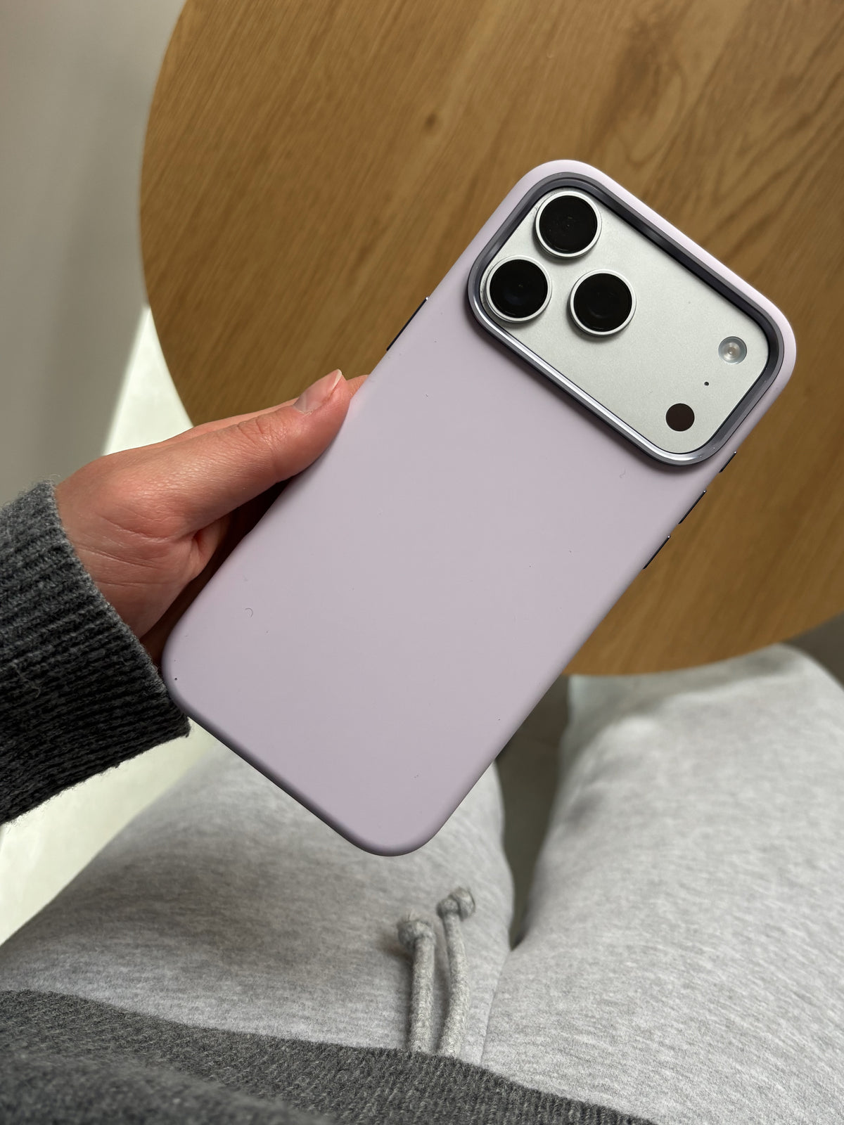 Лавандово-рожевий чохол на iPhone у руці на тлі дерев’яного столу