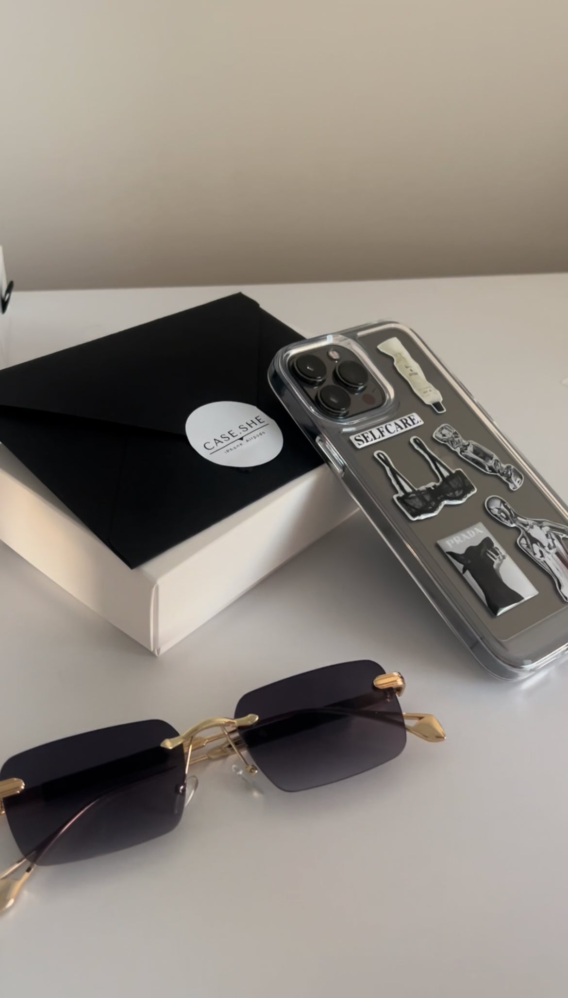 Наліпки «Self Care» на прозорому чохлі для iPhone поруч з окулярами й коробкою CASE.SHE