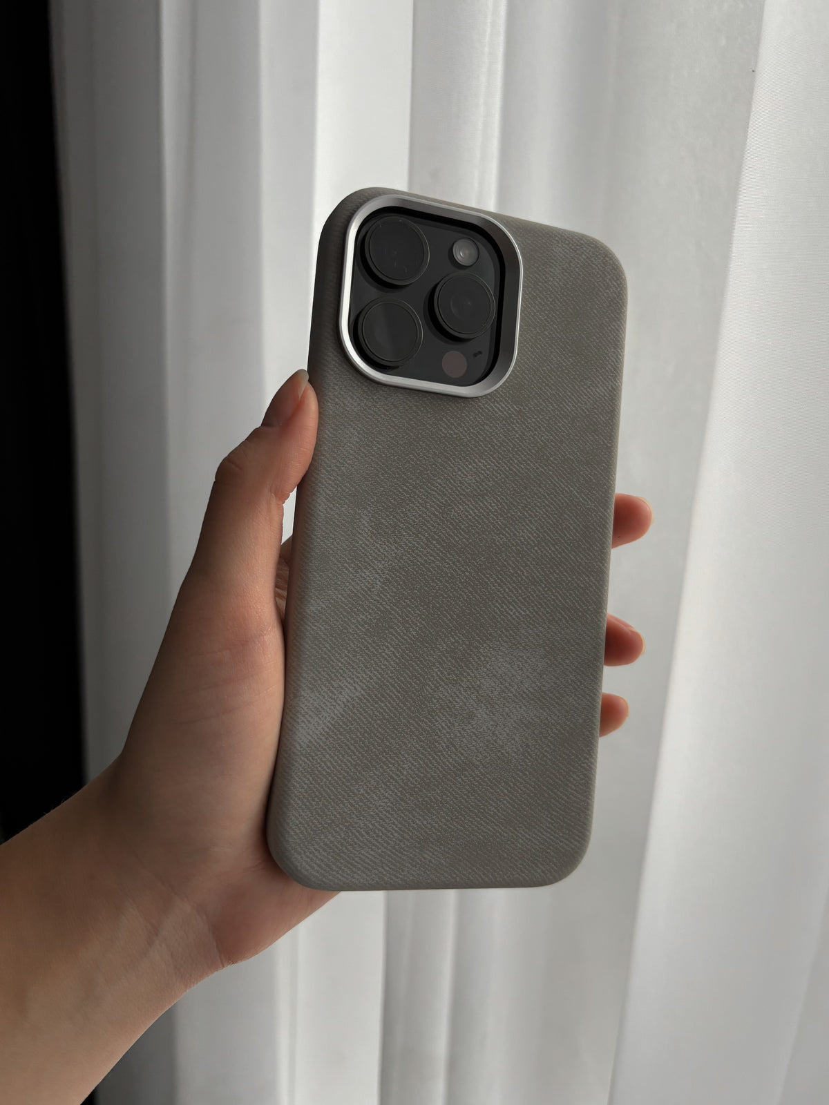 Сірий чохол на iPhone у руці біля білої фіранки