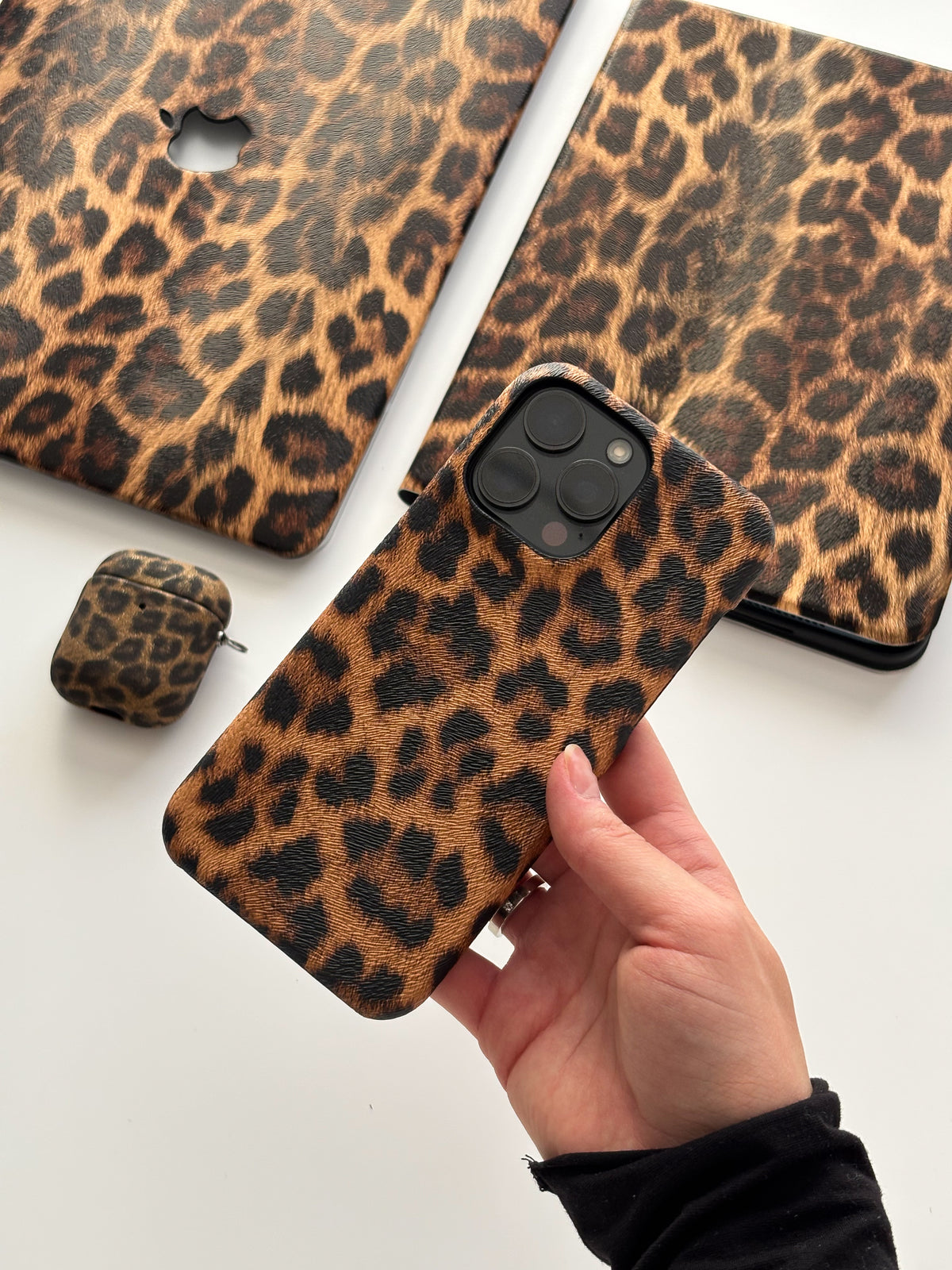 Леопардовий чохол на iPhone у руці на тлі леопардових чохлів для MacBook та AirPods