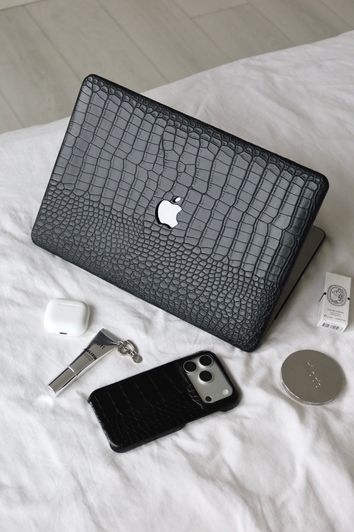 Чорний чохол Gator Skin на MacBook на білому ліжку поруч з iPhone, навушниками й аксесуарами