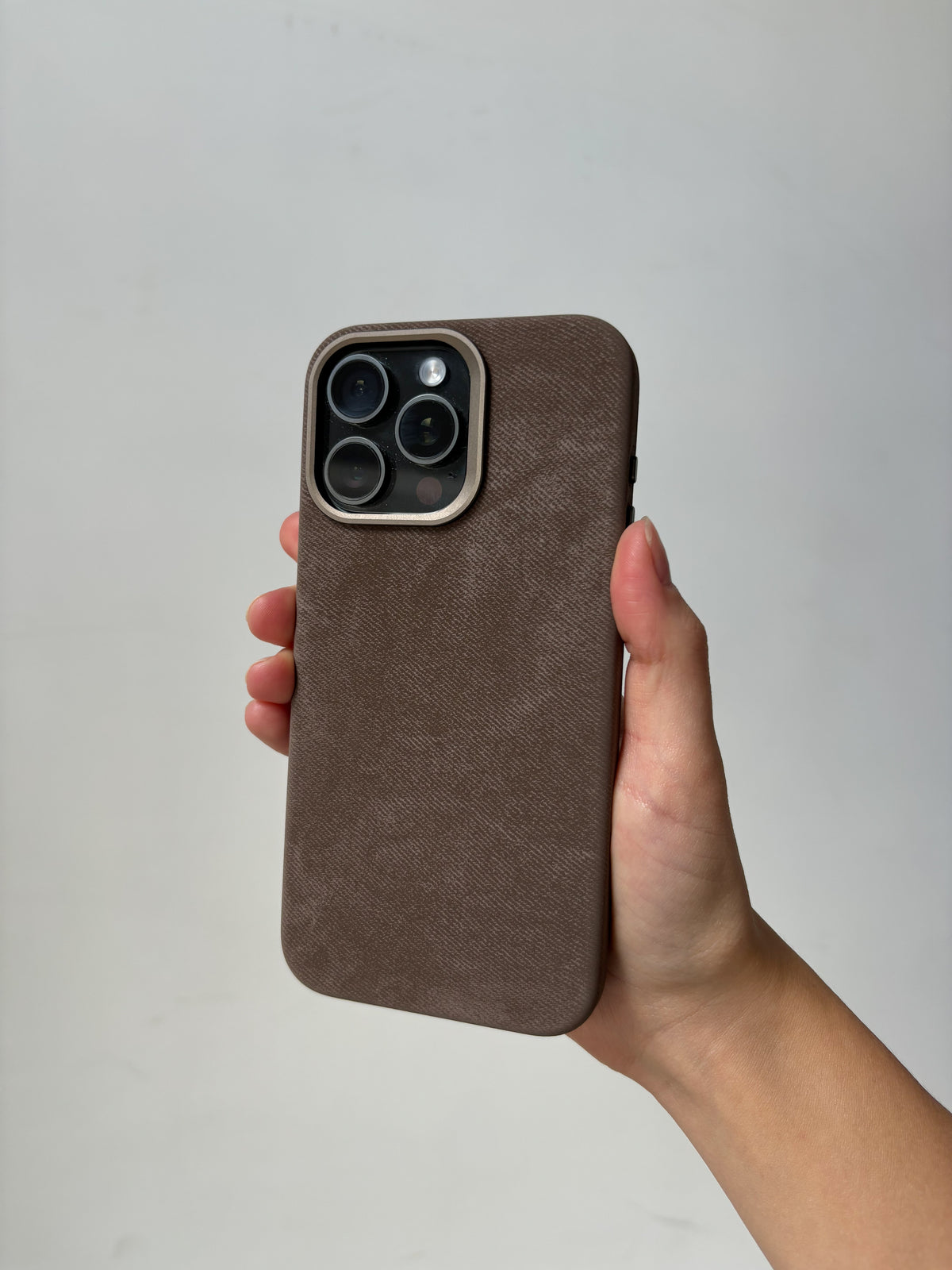 Коричневий чохол на iPhone з квадратним вирізом під камеру в руці