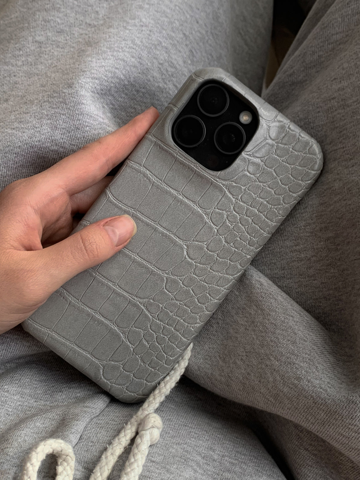 Сірий чохол Gator Skin на iPhone у руці на тлі сірого трикотажу