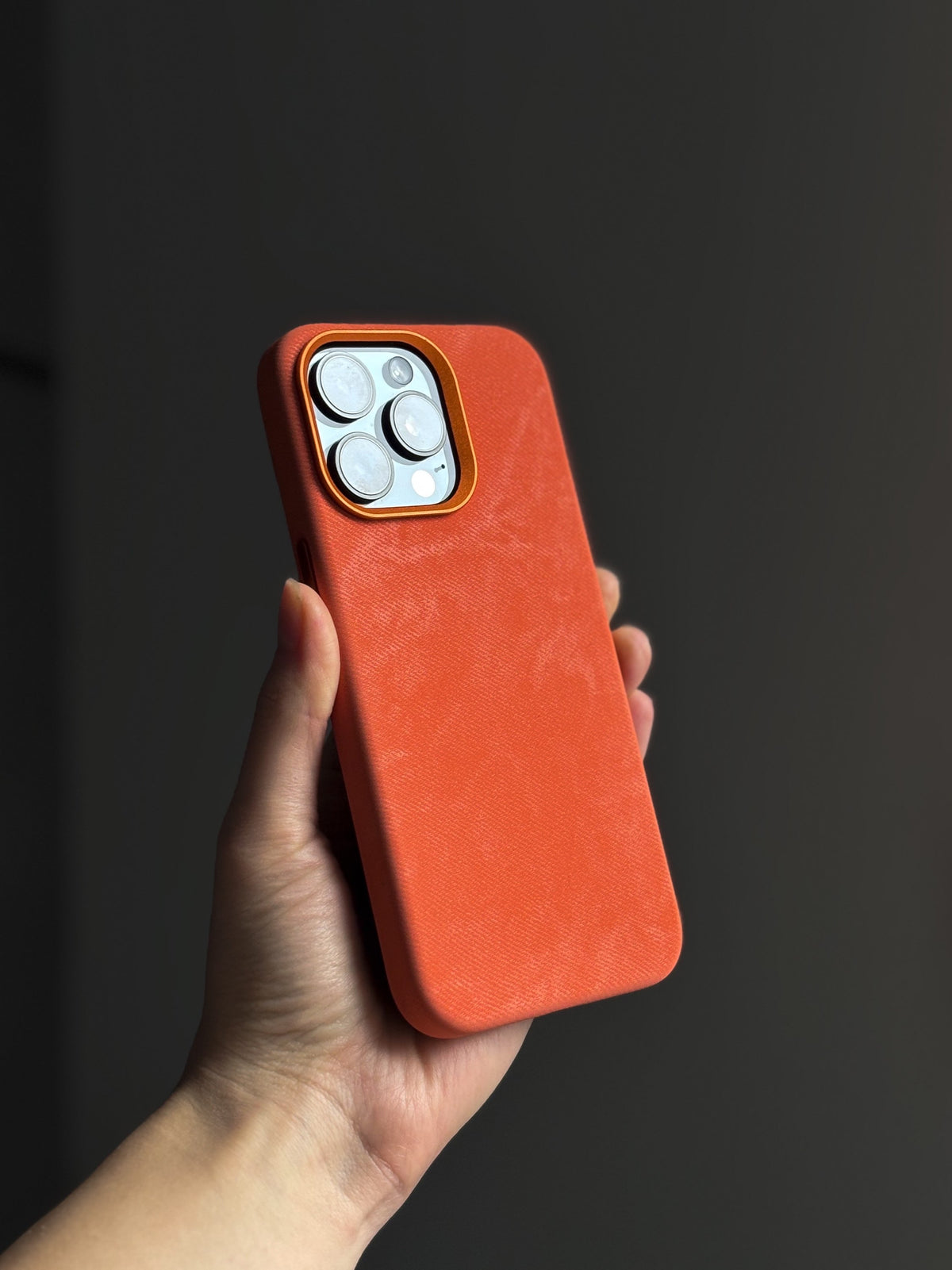 Помаранчевий чохол на iPhone зі світлими камерами в руці на темному тлі