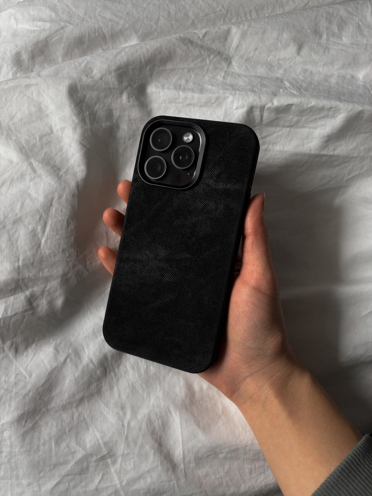 Чорний чохол на iPhone у руці на тлі білої постільної білизни