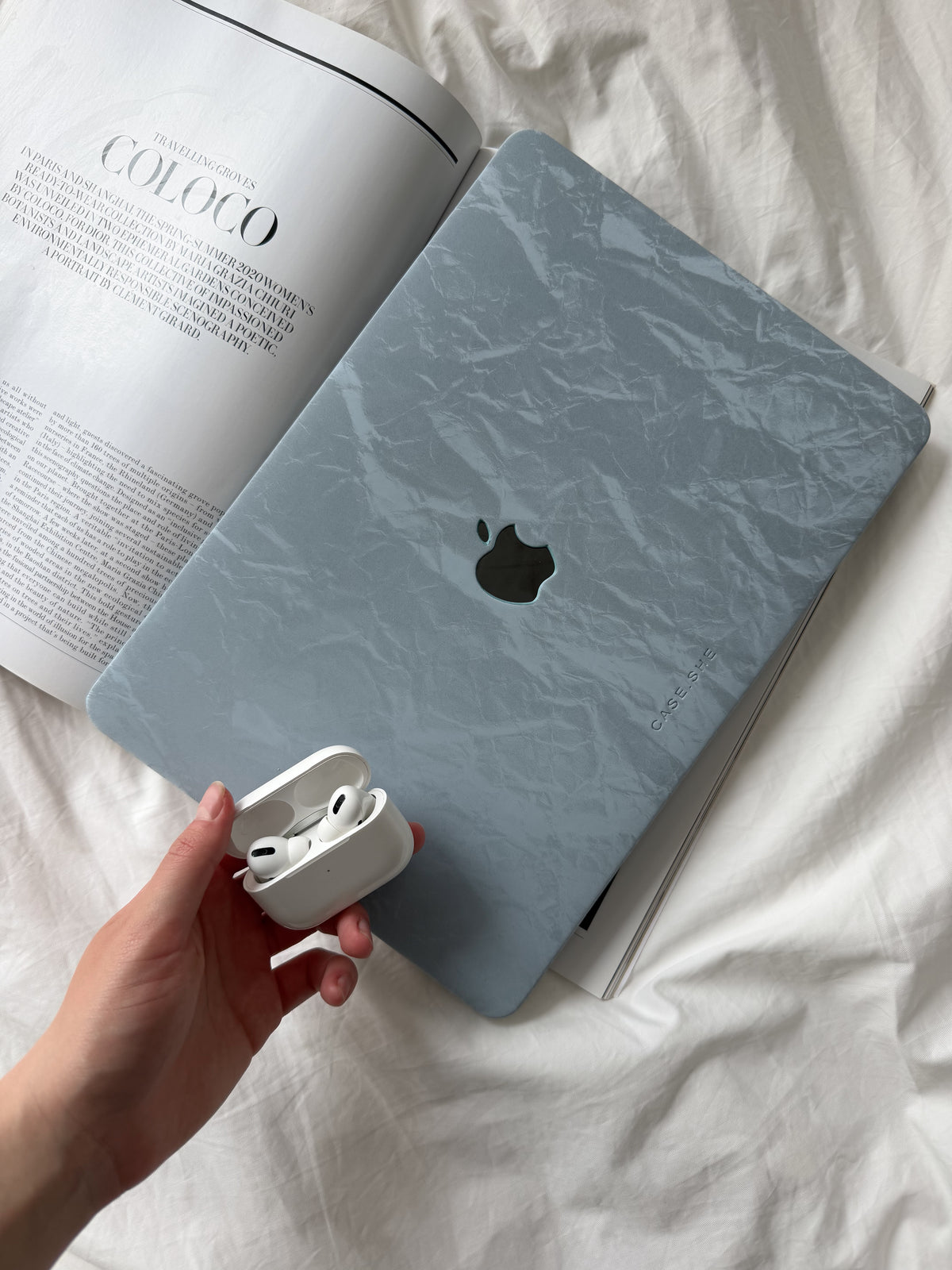 Блакитний чохол-накладка «Оксамит» для MacBook із фактурою заломів на ліжку поруч із журналом і навушниками