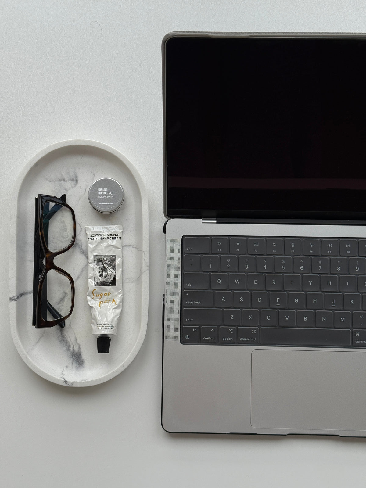 Відкритий MacBook у чохлі «Замшева м’якість» поруч із мармуровою тацею з окулярами