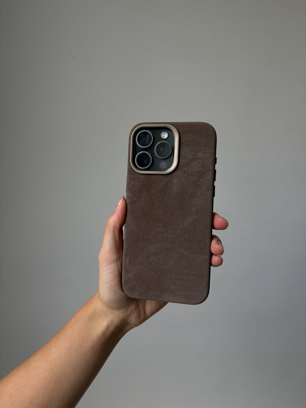 Коричневий чохол «Замшева м’якість» на iPhone у витягнутій руці на сірому тлі