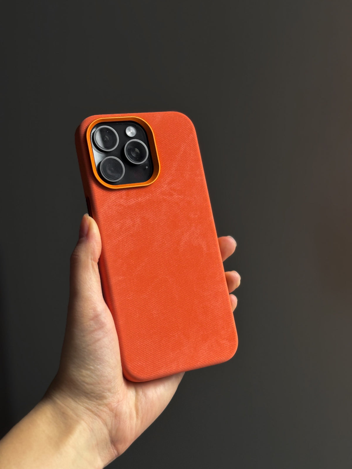 Помаранчевий чохол на iPhone з темними камерами в руці на темному тлі