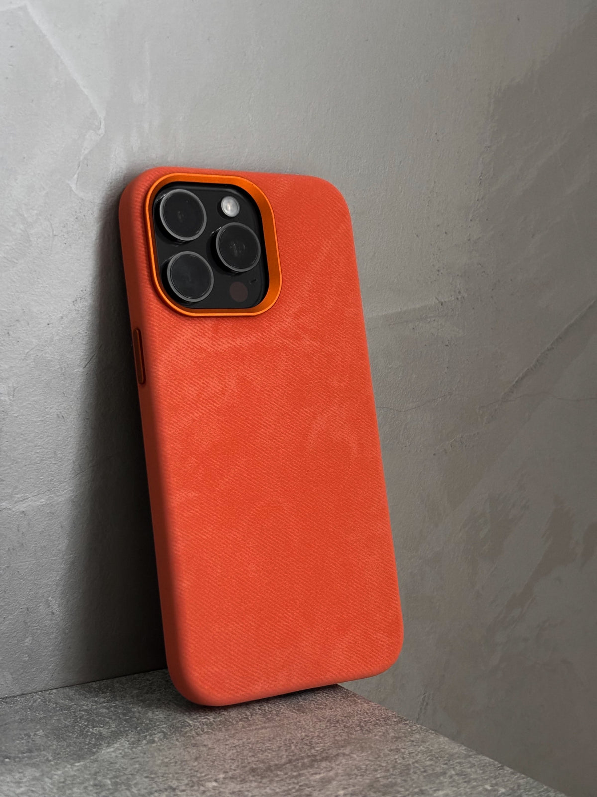 Помаранчевий чохол на iPhone стоїть біля бетонної стіни