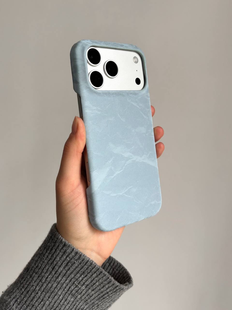 Блакитний чохол «Оксамит» на iPhone у витягнутій руці на сірому тлі