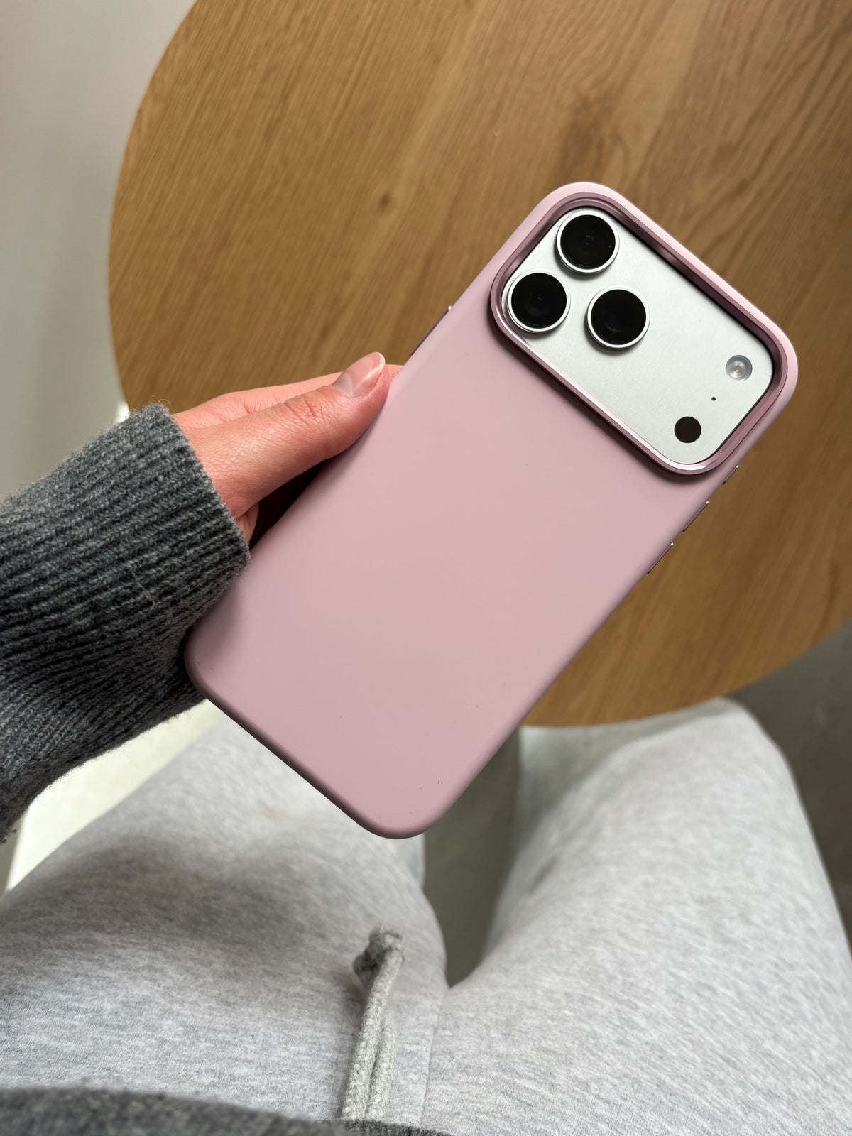 Рожевий чохол на iPhone у руці на тлі дерев’яного столу