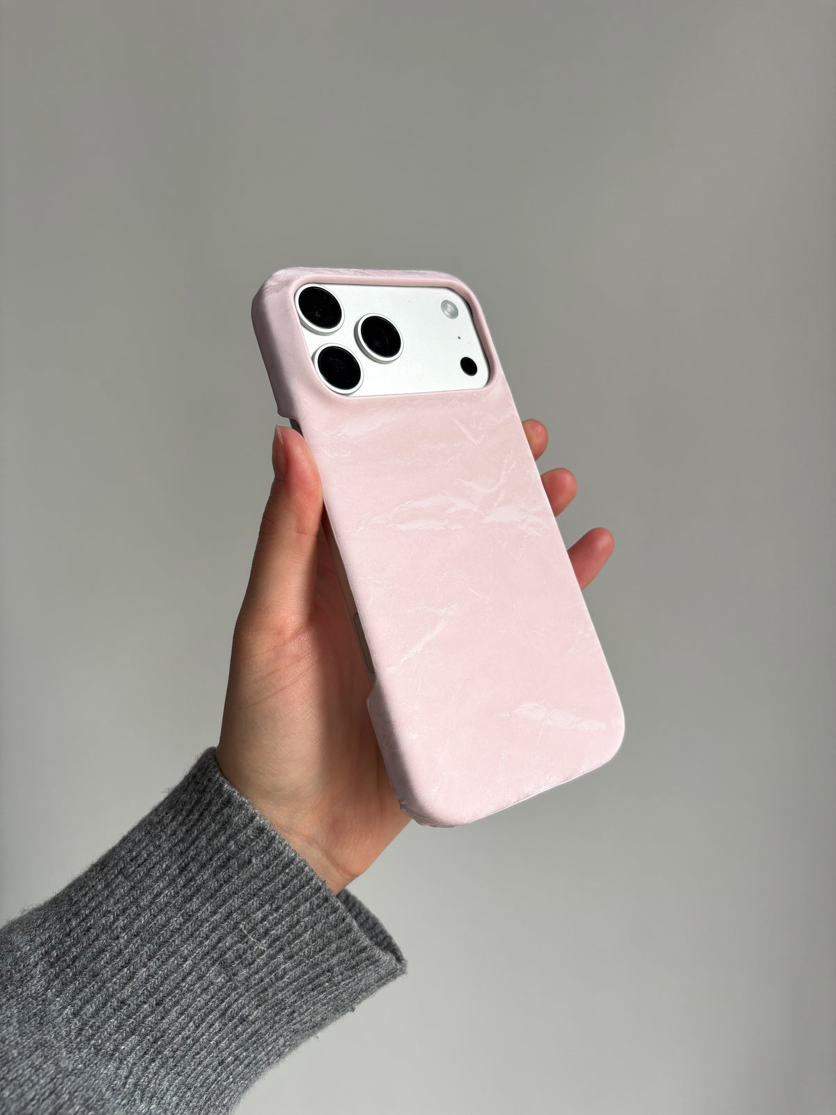 Рожевий чохол «Оксамит» на iPhone у витягнутій руці на сірому тлі